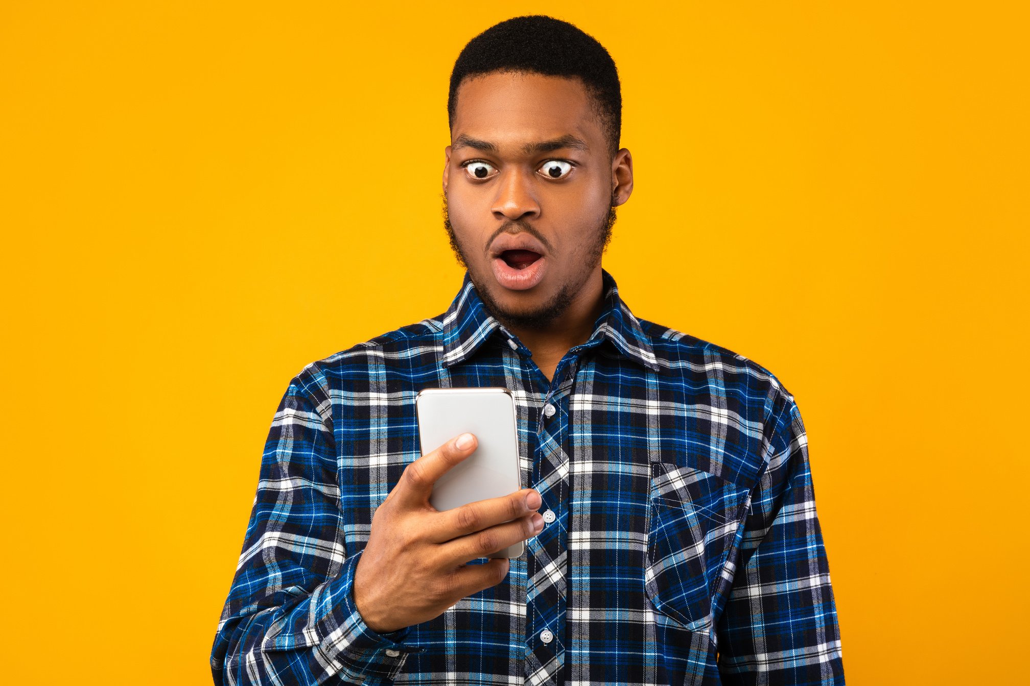 Shocked Black Man Looking At Smartphone Reading SMS, Yellow Background